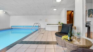 Ein Schwimmbad mit gefliestem Boden, ein Empfangsbereich mit Theke und Sitzgelegenheiten sowie ein Korbtisch mit Flasche und Gläsern.
