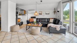 Ein modernes Wohnzimmer mit Kamin, einer schwarzen Ledersofa, einem Holztisch und einem großen Fenster mit Blick ins Freie.