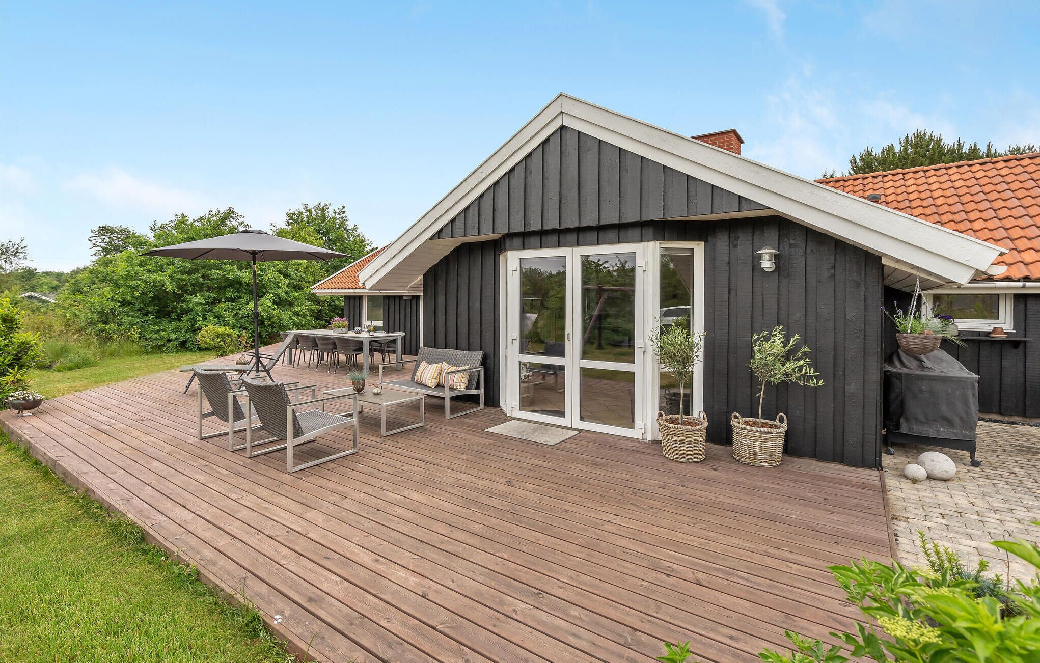 Ett modernt hus med en träaltan, en matplats med utemöbler och en stor skjutdörr i glas.