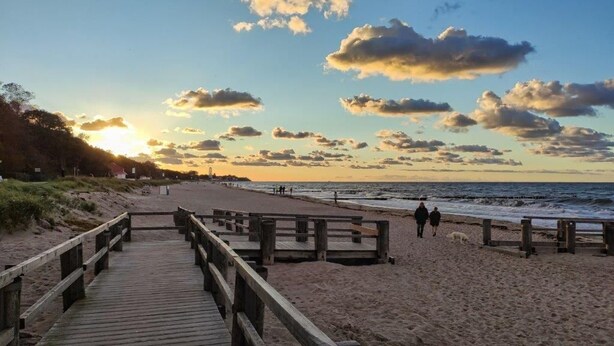 Un muelle de madera que conduce a una playa con un atardecer de fondo.