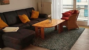 Una sala de estar con un sofá, una mesa de centro de madera y un sillón de mimbre.