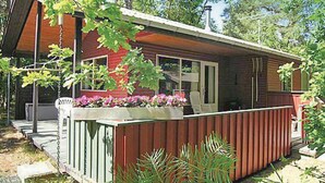 A small, single-story cabin with a porch, a small deck, and a window overlooking a garden.