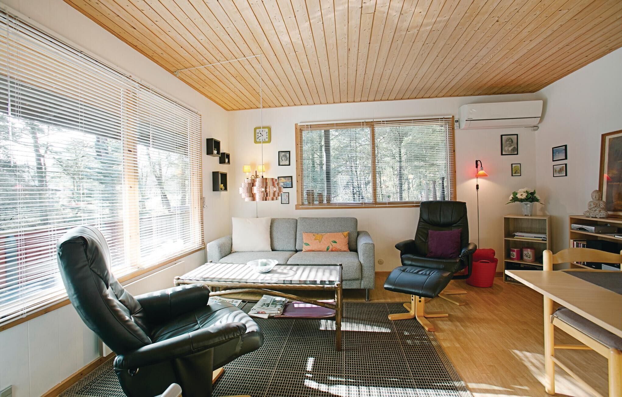 Un salon chaleureux avec un plafond en bois, un canapé, un fauteuil en cuir noir, une table basse et une bibliothèque.