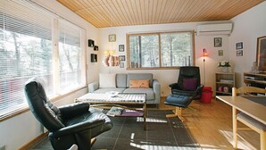 A cozy living room with a wooden ceiling, a sofa, a black leather chair, a coffee table, and a bookshelf.