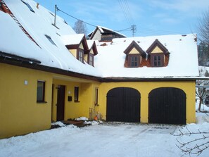 A yellow building with two black garage doors and a sloped roof covered in snow. - Three Peaks - Ferienhof High (Hiltpoltstein)