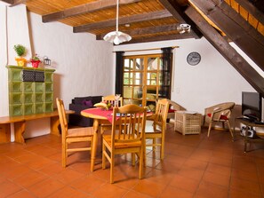 Zona pranzo con mobili in legno, un contenitore portaoggetti verde e una televisione.