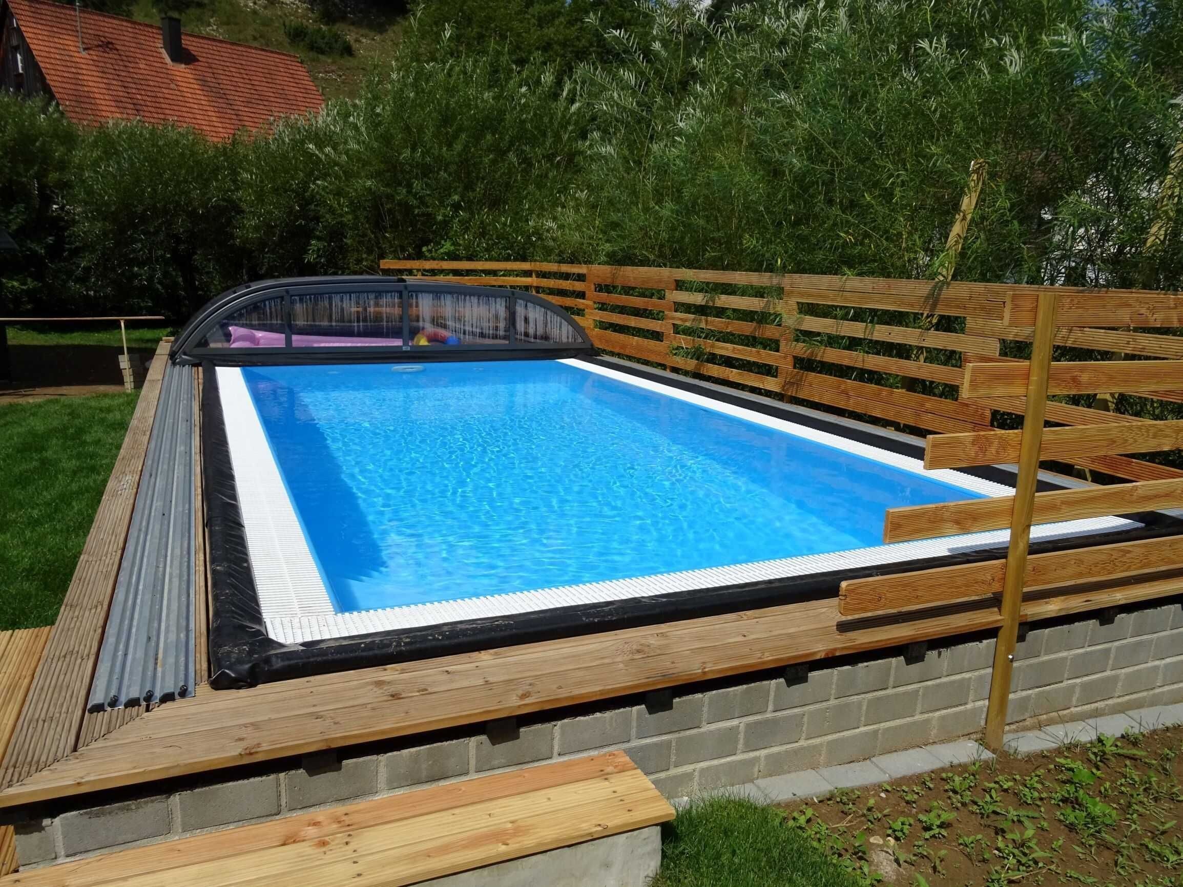 A rectangular swimming pool with a wooden deck and a brick wall.