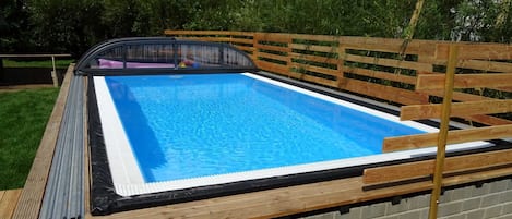 En rektangulär swimmingpool med ett trädäck och en mur av tegelsten.