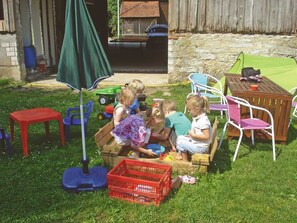 Children playing in a wooden playhouse with a green umbrella, surrounded by outdoor furniture and a stone wall. - Three Peaks - Ferienhof High (Hiltpoltstein)