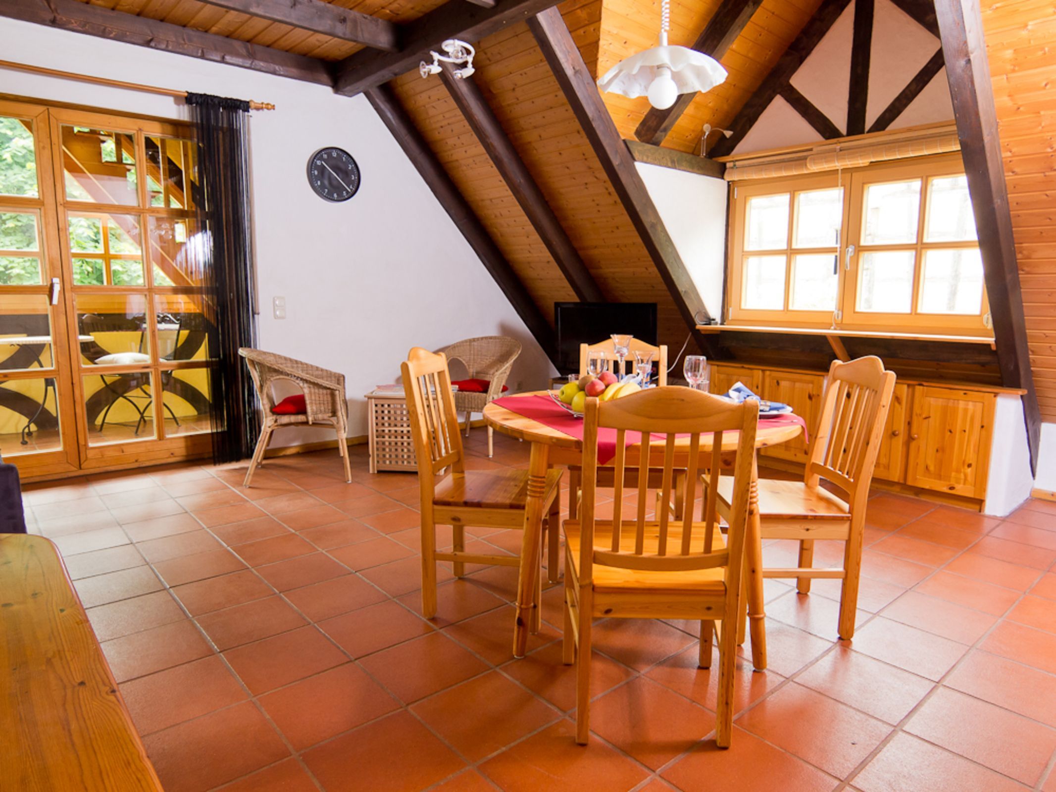 Ein Essbereich mit einem runden Tisch, Holzstühlen, einer Uhr an der Wand und großen Fenstern.