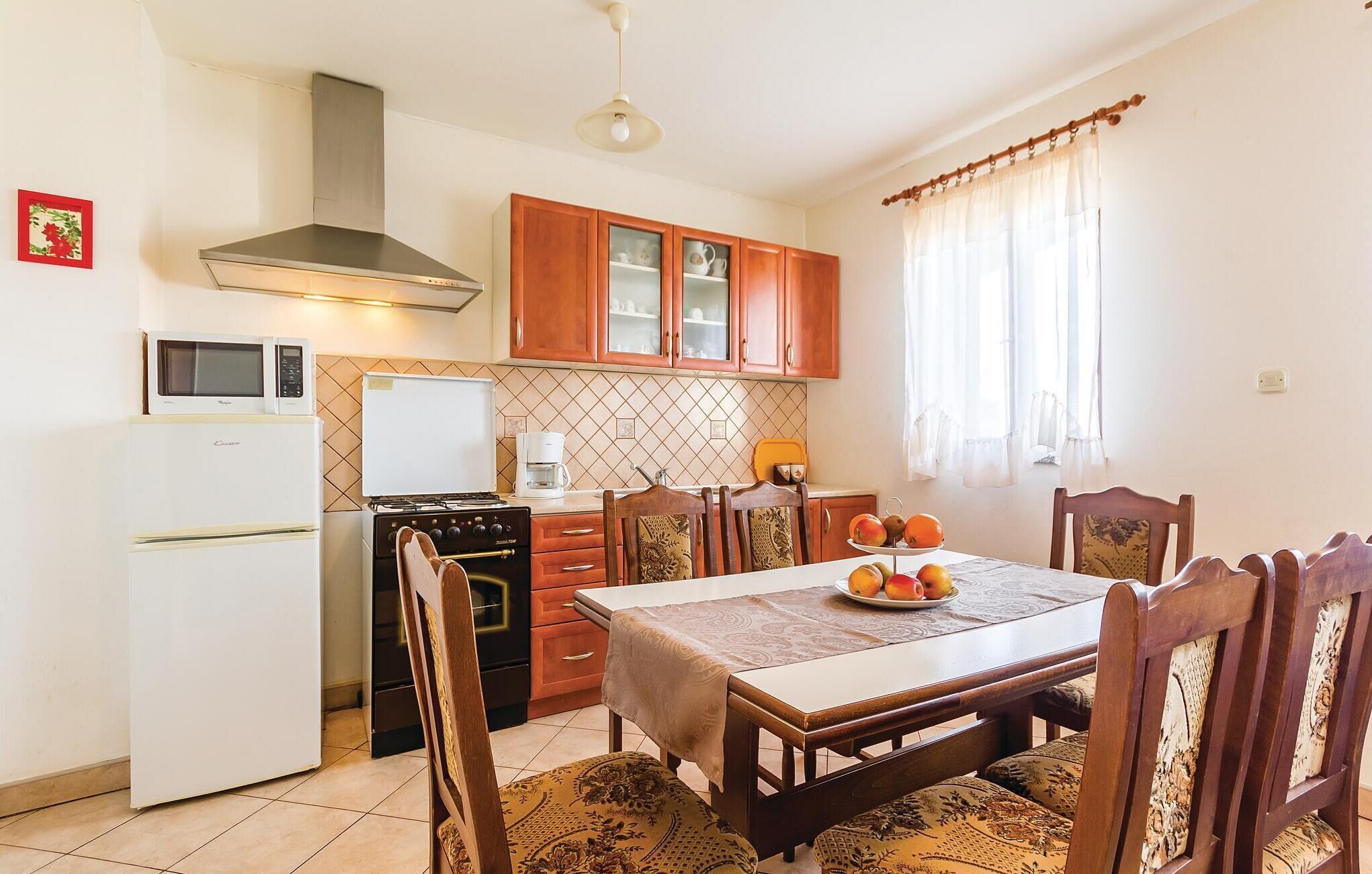 Une cuisine compacte équipée d’une cuisinière, d’un four à micro-ondes et d’un réfrigérateur. On y trouve une table à manger avec des chaises et une assiette de fruits.