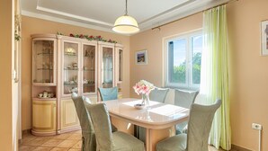 Un comedor con mesa, sillas, una alacena con puertas de cristal y una ventana con cortinas.