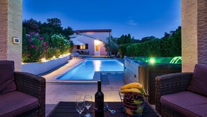 Zona de piscina con sillones reclinables, un jacuzzi y una mesa con copas de vino y fruta.