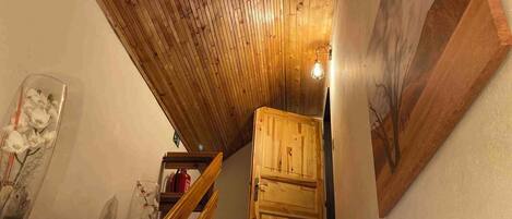 Una escalera de madera que lleva a un altillo con techo inclinado y una puerta de madera.
