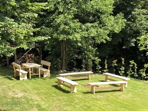 A wooden picnic table and chairs set in a grassy area with trees in the background.