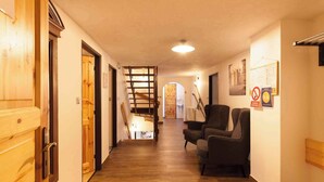 Un couloir doté d’un plancher en bois, d’un escalier et d’un coin salon avec un fauteuil.