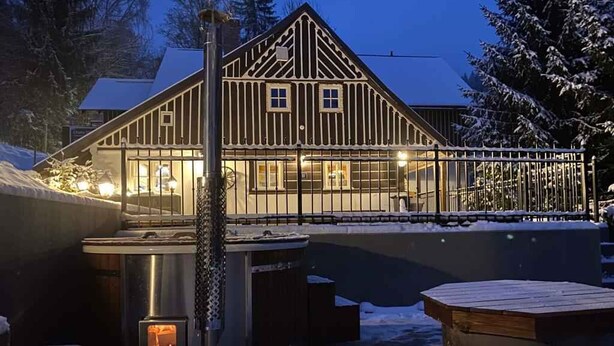 Une cabane en bois dotée d’une grande fenêtre, d’un bain à remous et d’un espace extérieur aménagé avec des sièges.