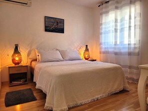 Ein Schlafzimmer mit einem Bett, Nachttischen, einem Teppich, einem Gemälde und einem Fenster mit Vorhängen.