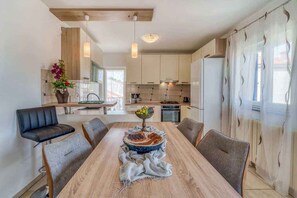 A modern kitchen with a dining area, featuring a wooden table, chairs, and a vase with flowers. - Holiday apartment with air conditioning (Porat)