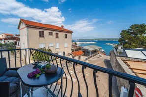 A balcony with a table, a building with a red roof, and a view of the sea and boats.