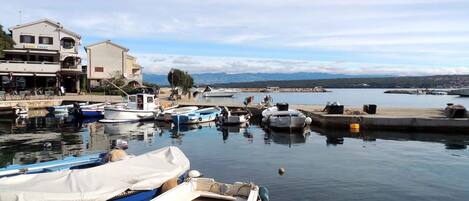 A marina with several boats docked, a building with a sign, and a view of the water and distant mountains.