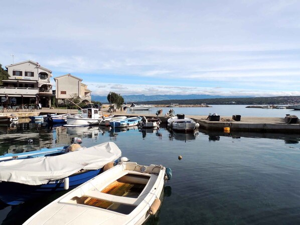 A marina with several boats docked, a building with a sign, and a view of the water and distant mountains.