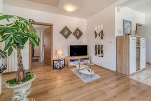 A living room with a flat-screen TV, wooden flooring, a potted plant, and a cabinet with drawers. - Holiday apartment with air conditioning (Porat)