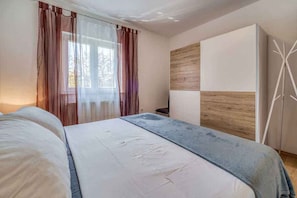 A bedroom with a bed, a bedside table, a wardrobe, and a window with curtains. - Holiday apartment with air conditioning (Porat)