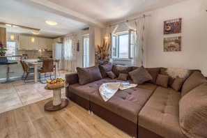 Ein modernes Wohnzimmer mit einem braunen Sofa, einem Couchtisch mit Obst und Blick auf die Küche und den Essbereich.