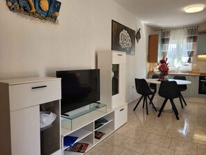 Ein modernes Wohnzimmer mit einem Flachbildfernseher, einem Glastisch und einem Essbereich mit Stühlen.