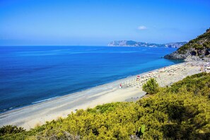 Une plage avec une eau d’un bleu limpide, un rivage sablonneux et une falaise rocheuse.