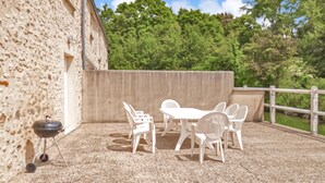 A patio with a white table and chairs, a barbecue grill, and a view of trees and a building in the background. - Lovely home in Vaudoy-en-Brie with WiFi (Vaudoy-en-Brie)