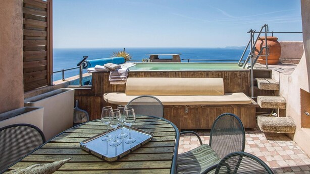 Une terrasse extérieure avec une table en bois, des chaises, un banc et une vue sur la mer.