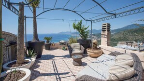 Une terrasse extérieure aménagée avec des sièges, des plantes en pot et une vue sur la mer.