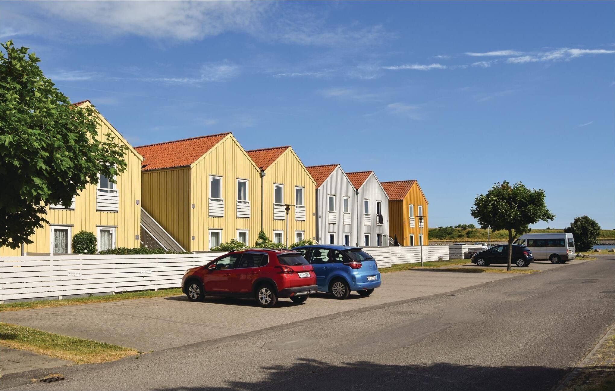Une rangée d’immeubles modernes à plusieurs étages, caractérisés par un style architectural uniforme, avec des toits recouverts de tuiles rouges et une clôture blanche en premier plan.