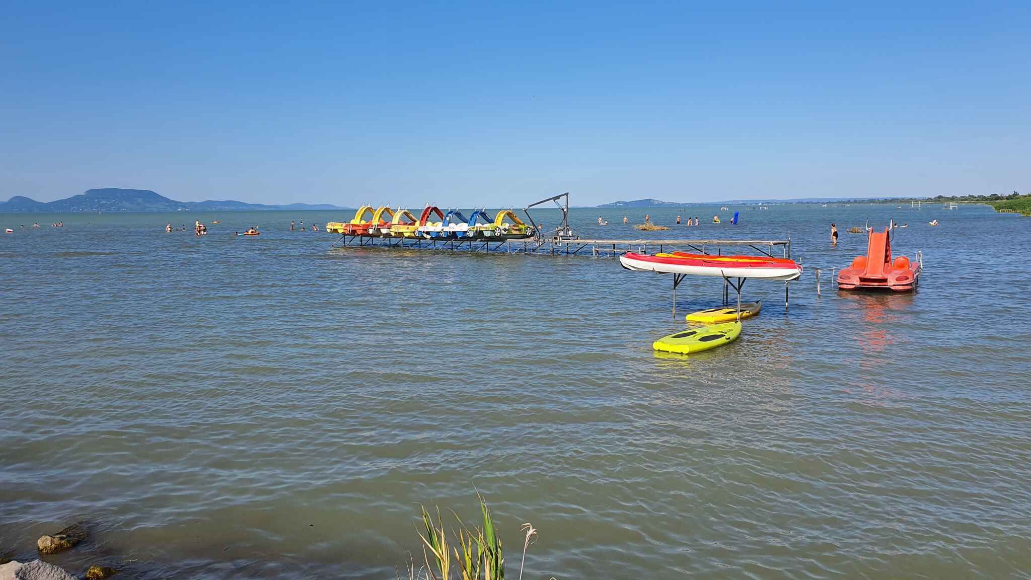 A lake with a dock, kayaks, and a small boat.