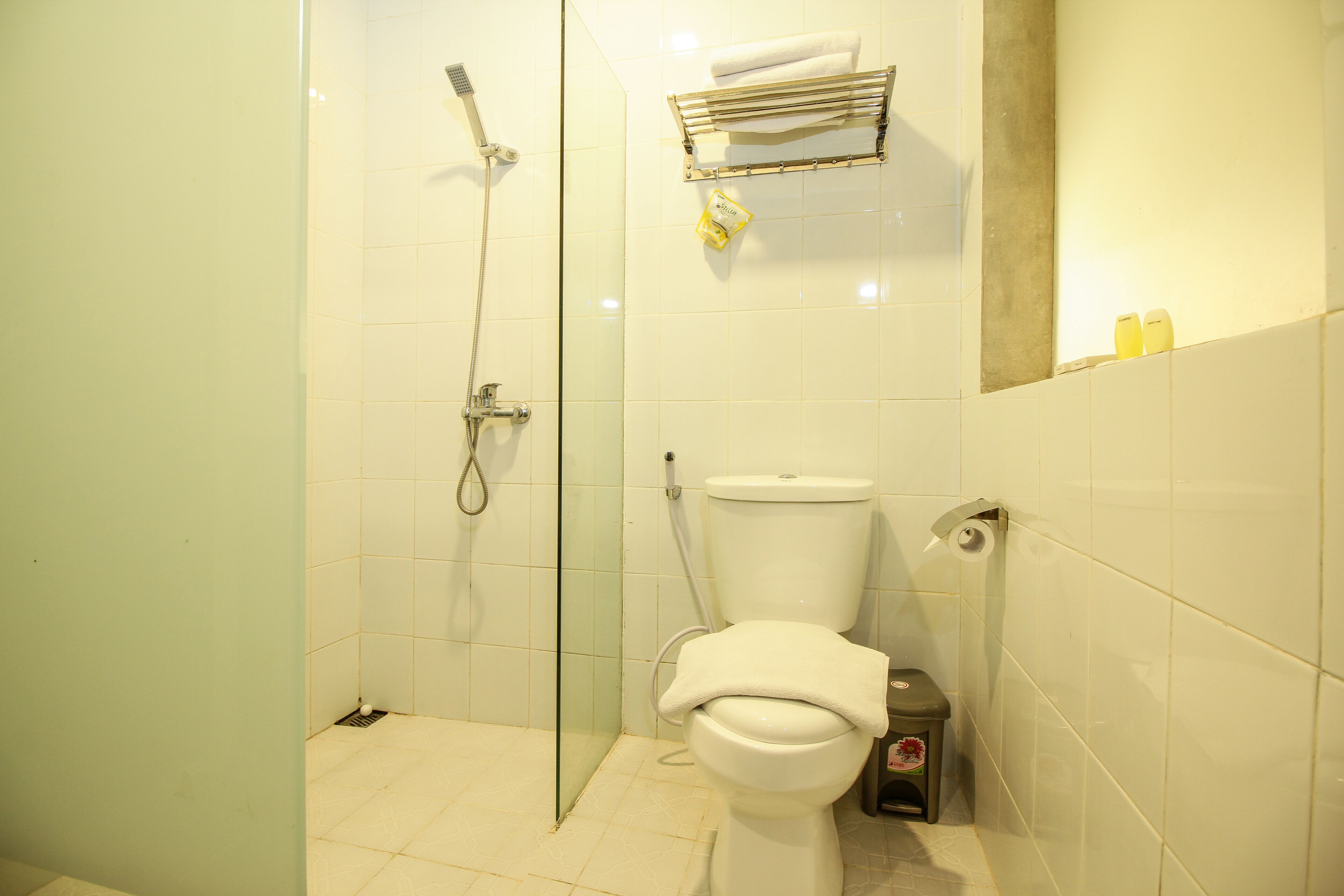 Une salle de bain avec une douche à parois de verre, des toilettes et une petite poubelle.