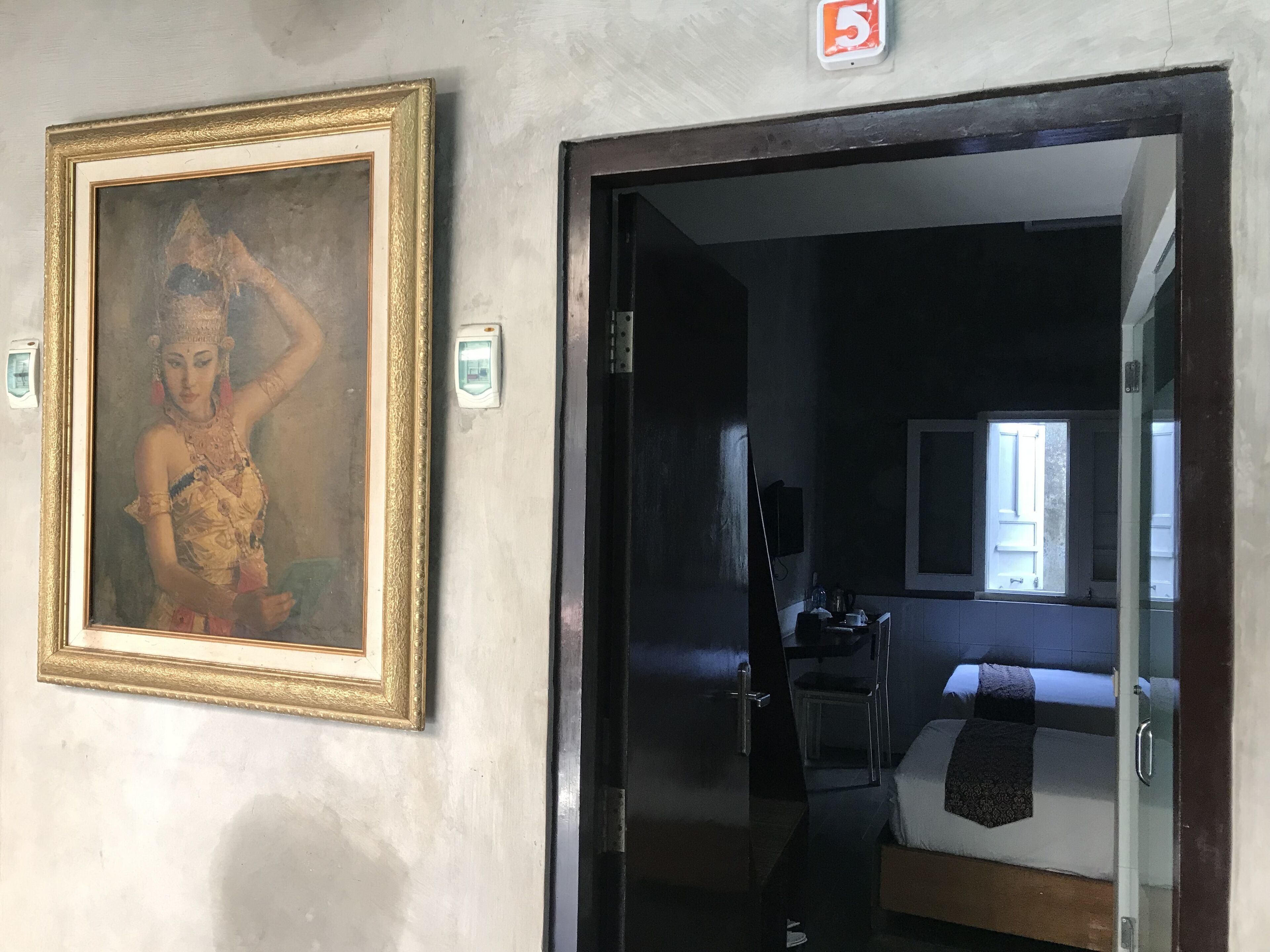 A hotel room with a bed, a window, and a painting on the wall.