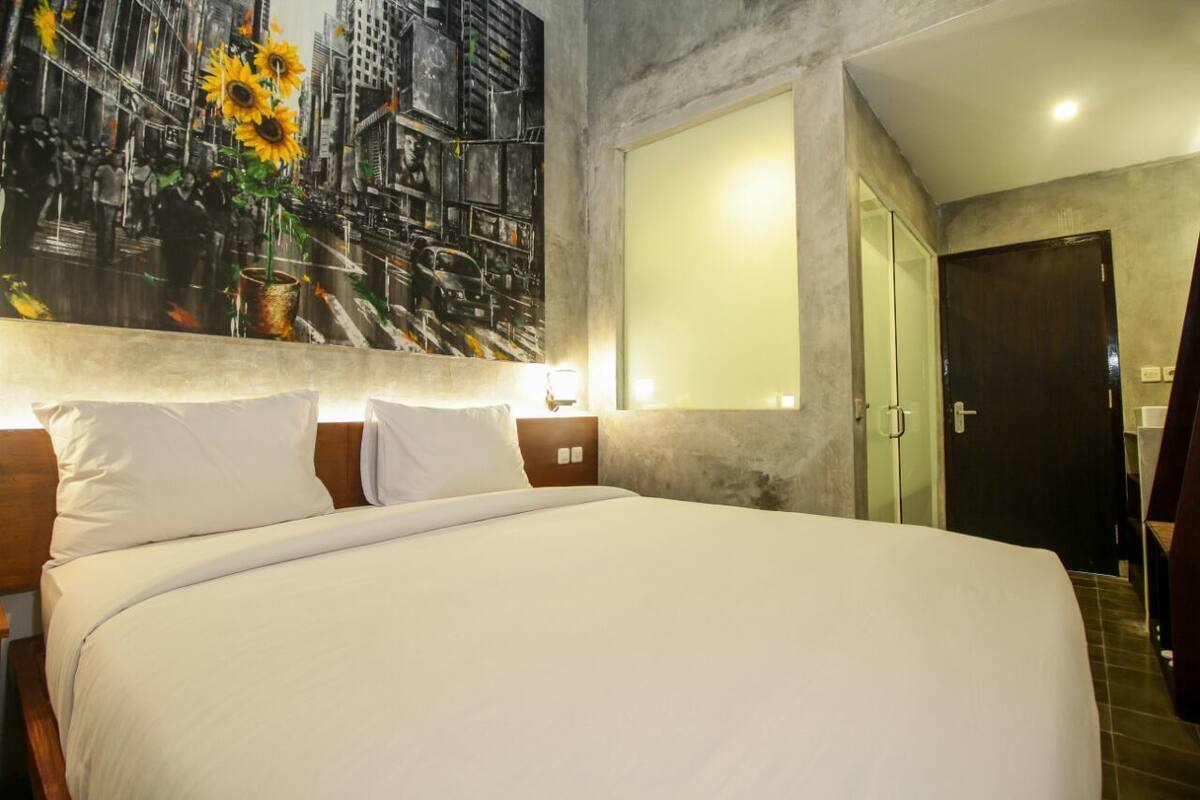 A hotel room with a large bed, a headboard with a cityscape mural, a glass door, and a plain wall.