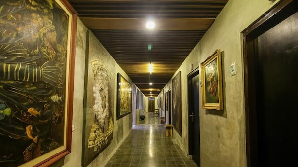 Um corredor com obras de arte emolduradas nas paredes, um banco de madeira e portas que dão para os quartos.