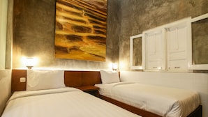 Quarto de hotel com duas camas de solteiro, uma grande pintura abstrata na parede e um espelho sobre a cama.