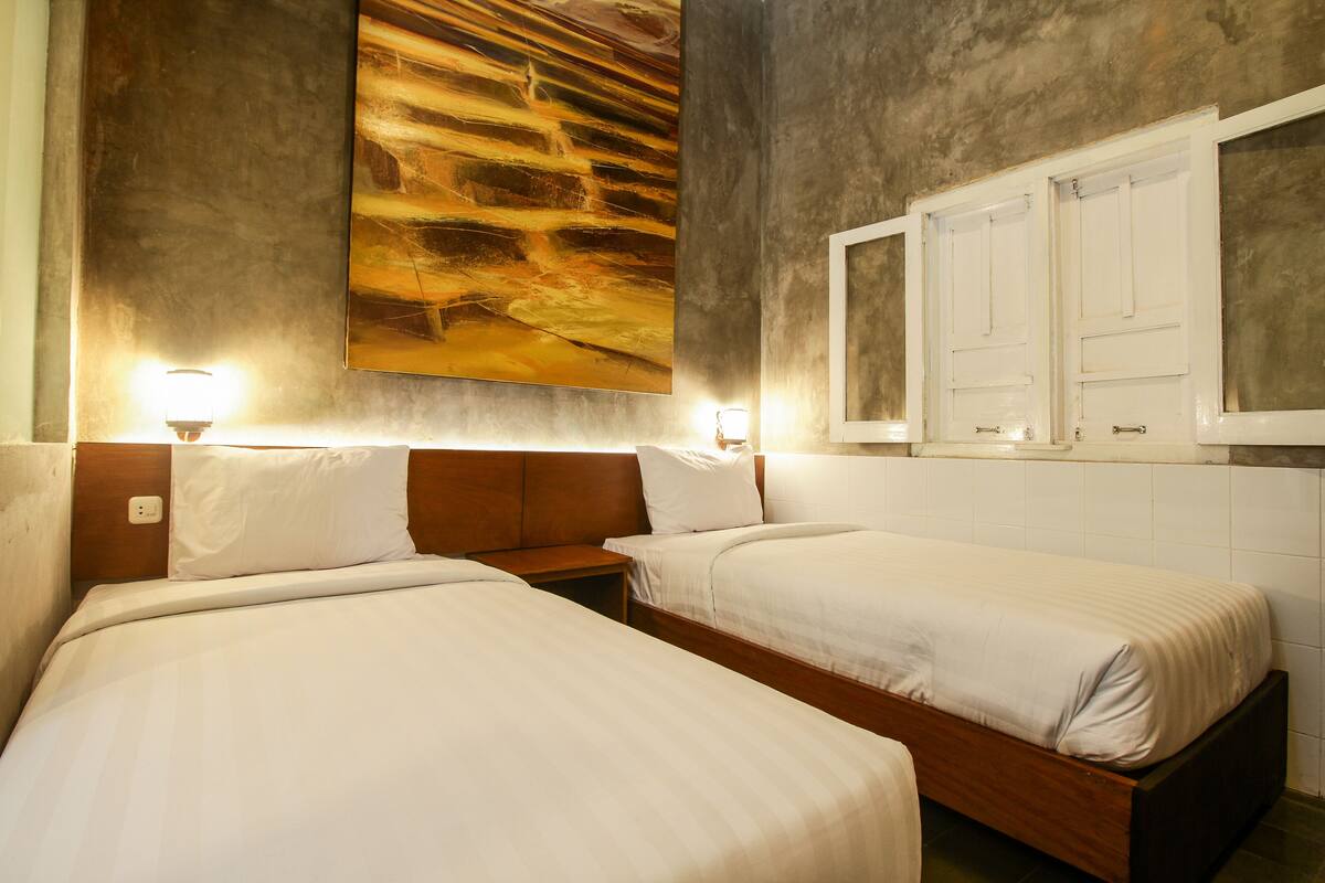 A hotel room with two single beds, a large abstract painting on the wall, and a mirror above the bed.