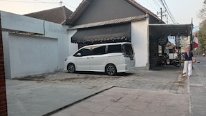 Uma carrinha branca estacionada numa entrada com um pátio ladrilhado e um acesso coberto.