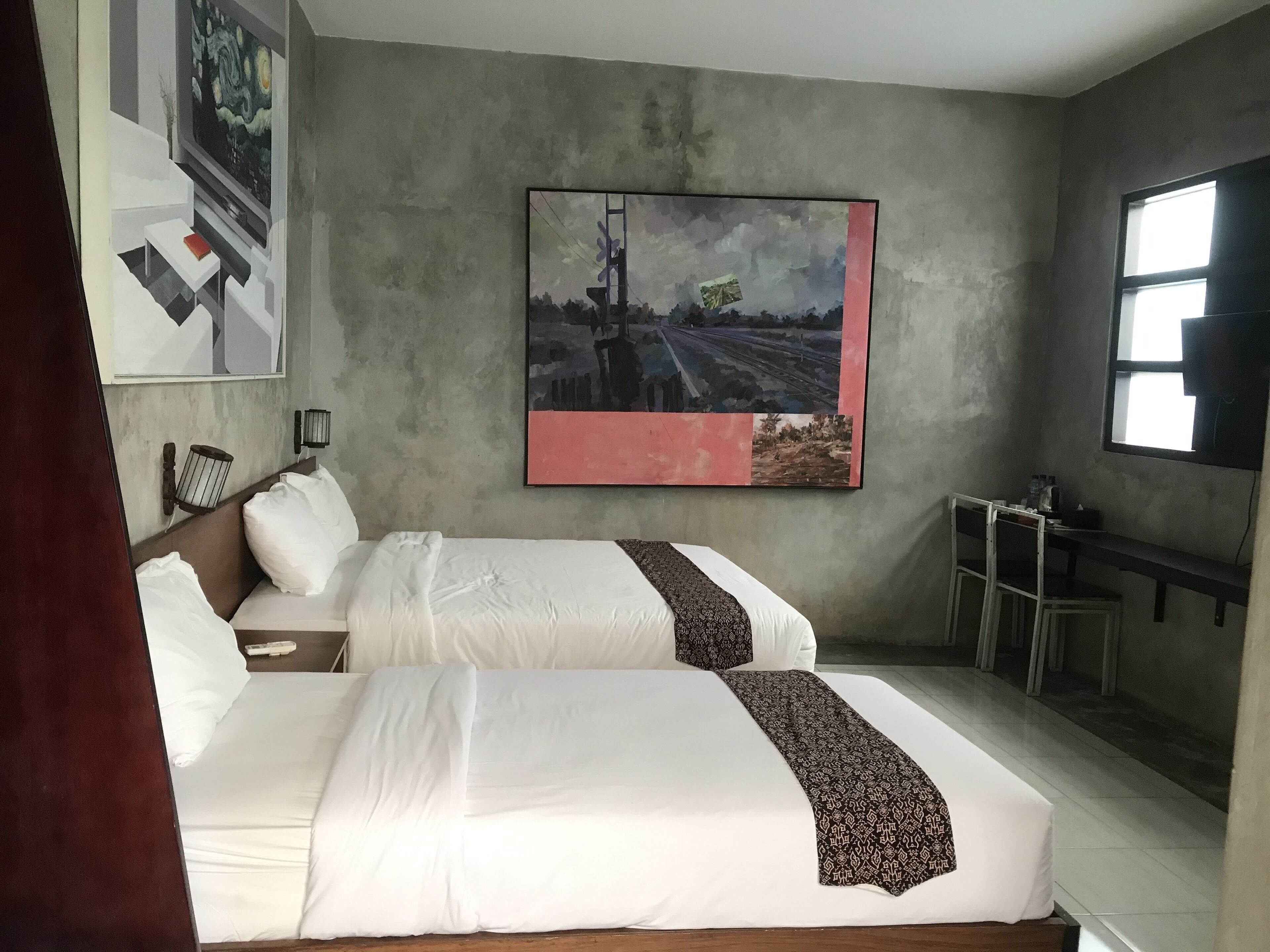 Habitación de hotel con dos camas, un cuadro grande en la pared, un escritorio con una silla y una ventana.