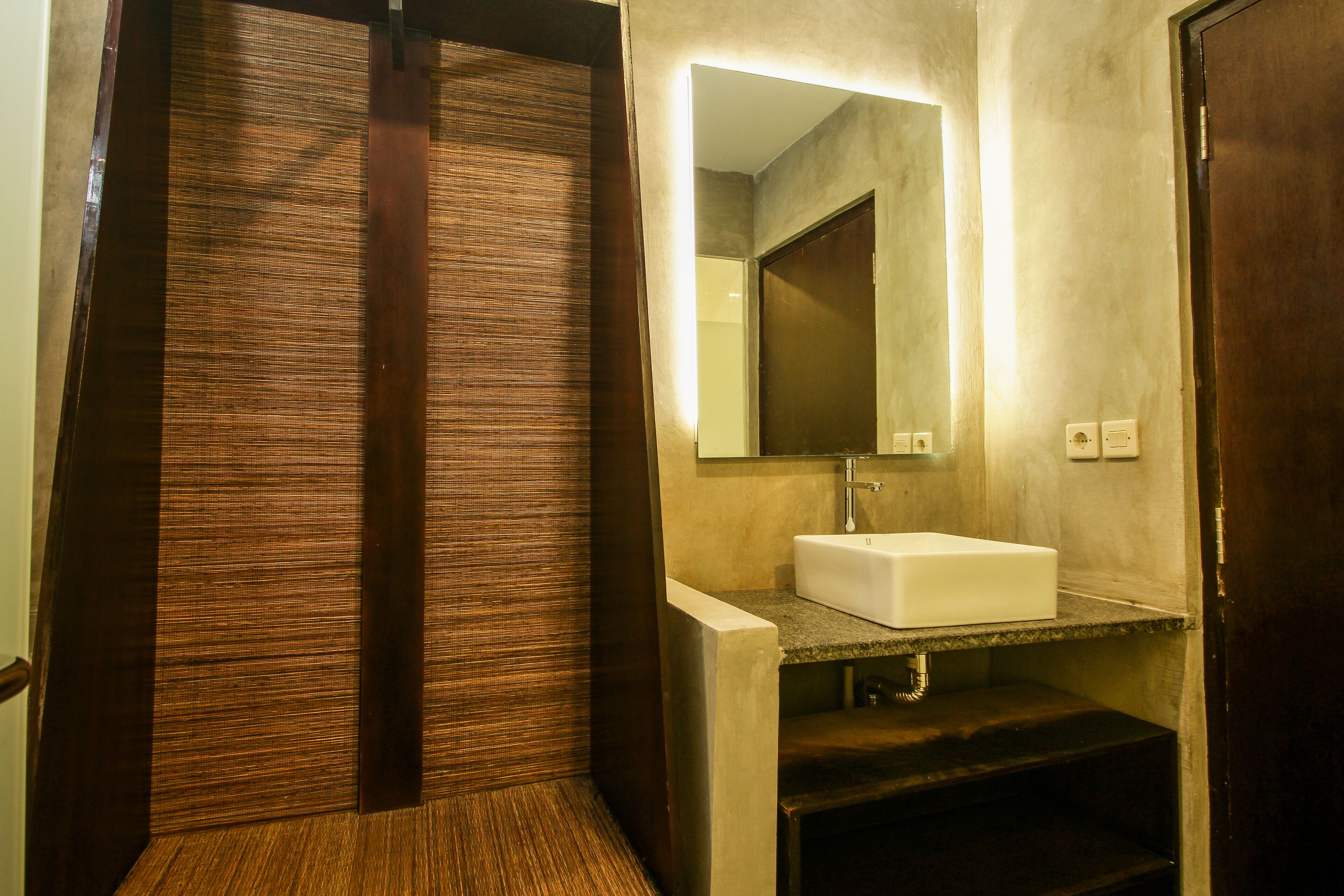 Un baño moderno con puerta de madera, un lavabo blanco y un espejo encima.