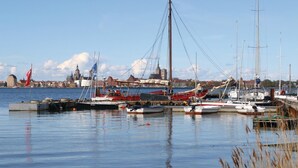 Een jachthaven met diverse boten afgemeerd, een heldere lucht en een stadsgezicht op de achtergrond.