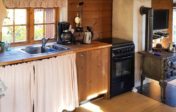 A kitchen with a wooden countertop, a sink, a stove, and a television.