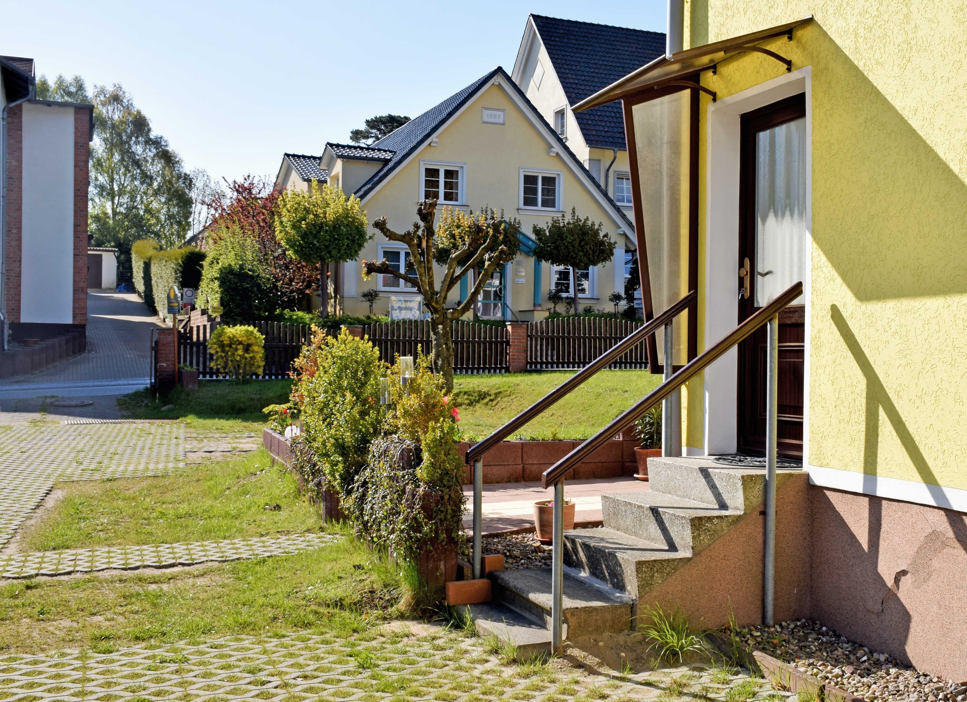 A residential area with a house featuring a staircase leading to the entrance, a paved driveway, and a well-maintained lawn.