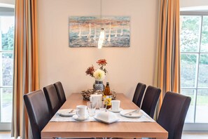 Une table à manger, avec des chaises, un vase de fleurs, une bouteille et un tableau accroché au mur.