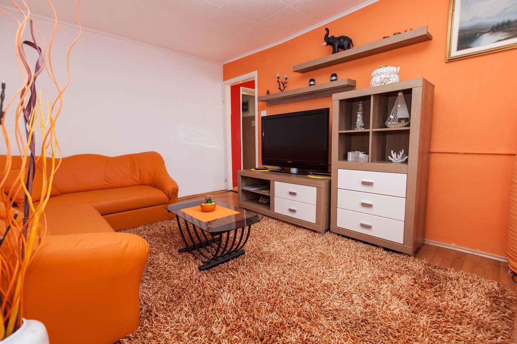 Ein Wohnzimmer mit einem orangefarbenen Sofa, einem Fernseher auf einem Holzboden und einem kleinen Tisch mit einer Vase.